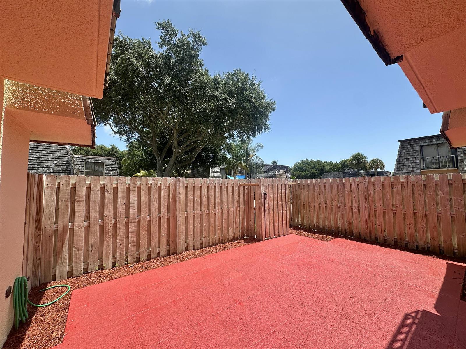 A fenced-in patio features a red painted concrete floor and a wooden gate — 255 Lake Arbor Drive, Palm Springs FL 33461, PALM SPRINGS, FL