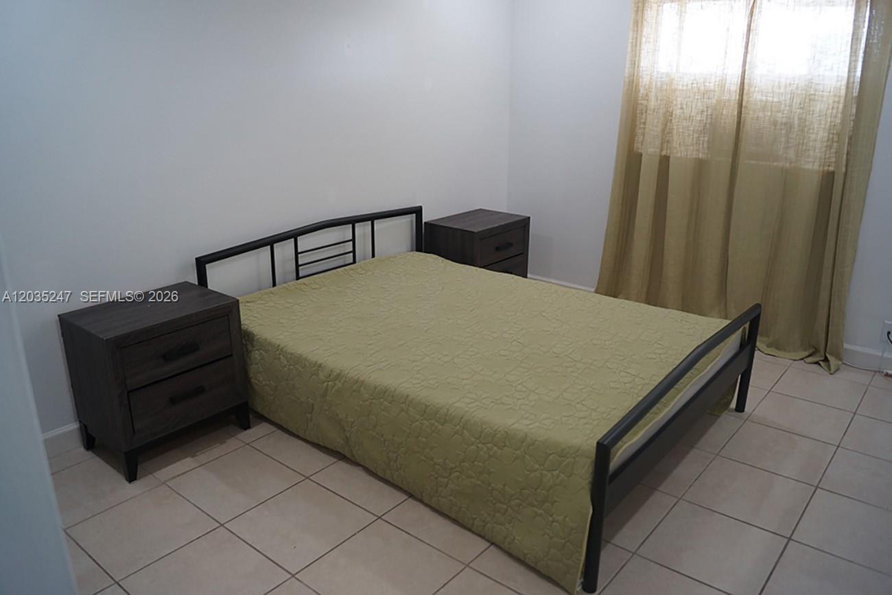 A bedroom features a metal bed frame, two dark wood nightstands, and beige curtains — 1250 E Sample Rd # 303, Pompano Beach FL 33064, POMPANO BEACH, FL