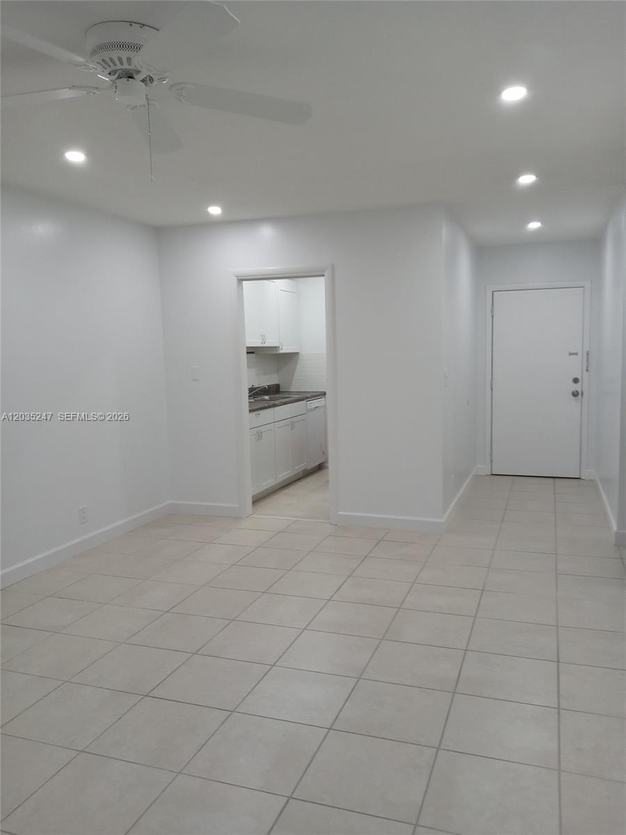 A bright, tiled room features a ceiling fan, recessed lighting, and a doorway to a kitchen — 1250 E Sample Rd # 303, Pompano Beach FL 33064, POMPANO BEACH, FL