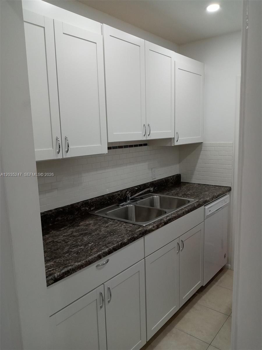 A galley kitchen features white shaker cabinets, a dark laminate countertop, and a double sink — 1250 E Sample Rd # 303, Pompano Beach FL 33064, POMPANO BEACH, FL