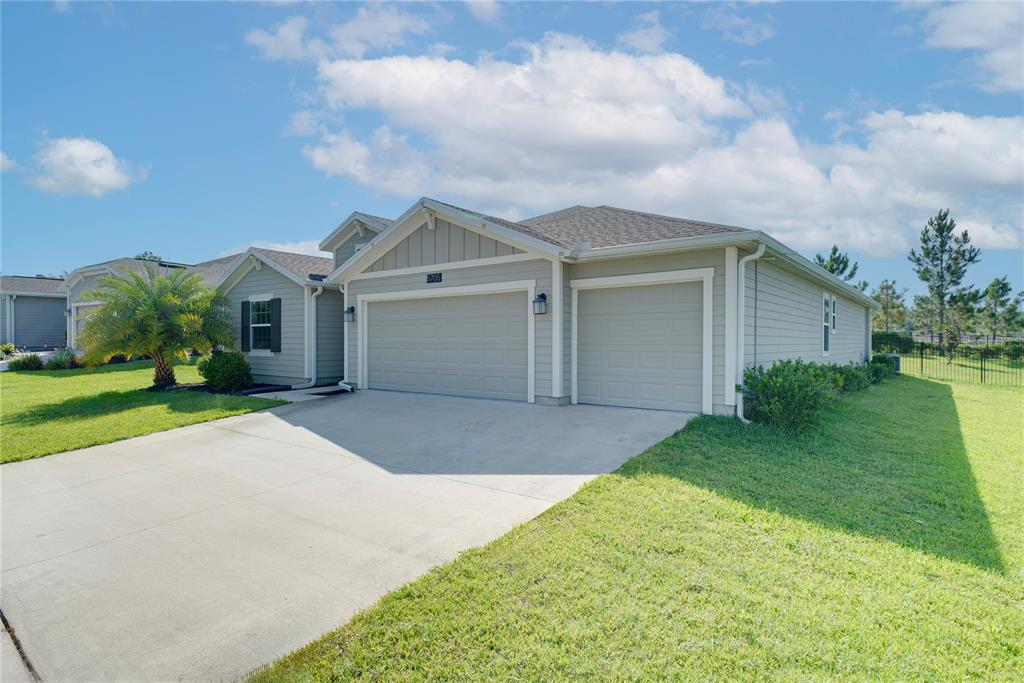 A light-colored single-story house features a three-car garage and a concrete driveway — 5705 ALENLON WAY, MOUNT DORA, FL