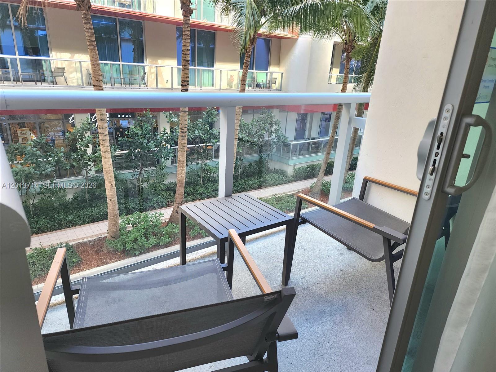 A balcony features two chairs and a small table overlooking a courtyard with palm trees — 777 N Ocean Dr # S207, Hollywood FL 33019, HOLLYWOOD, FL