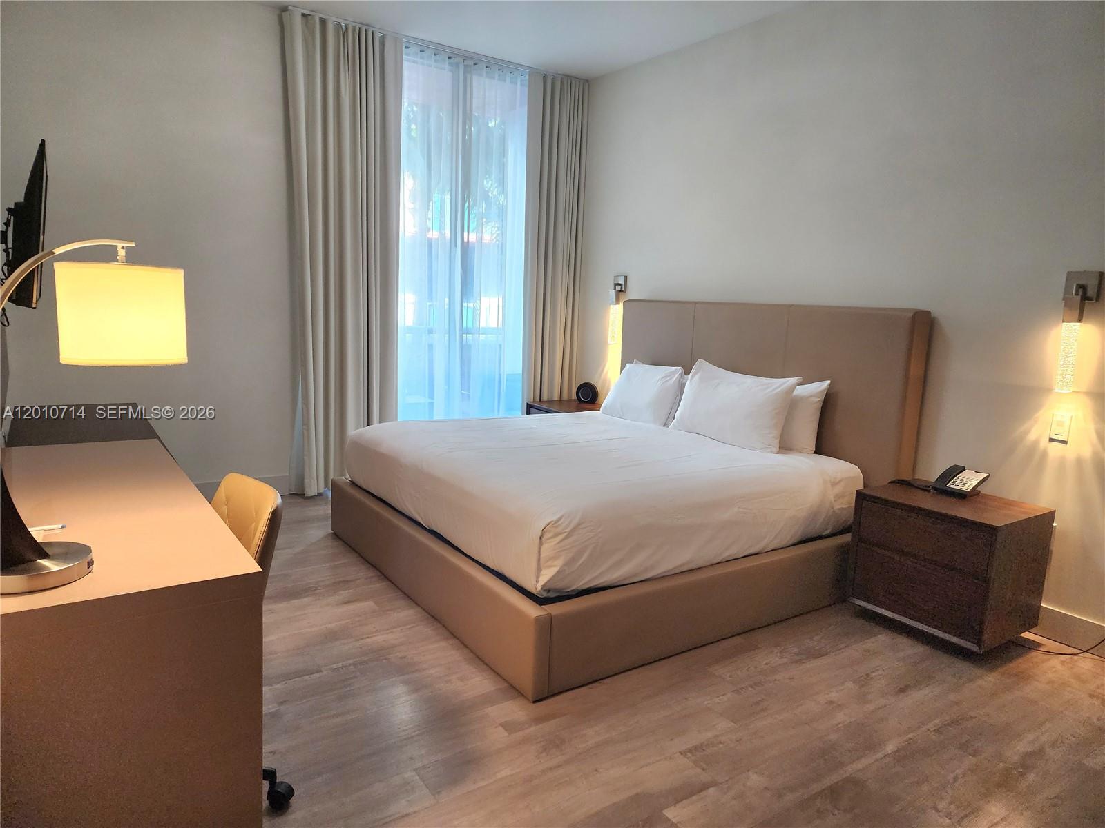 A bedroom features a platform bed, a desk, and floor-to-ceiling curtains over a window — 777 N Ocean Dr # S207, Hollywood FL 33019, HOLLYWOOD, FL