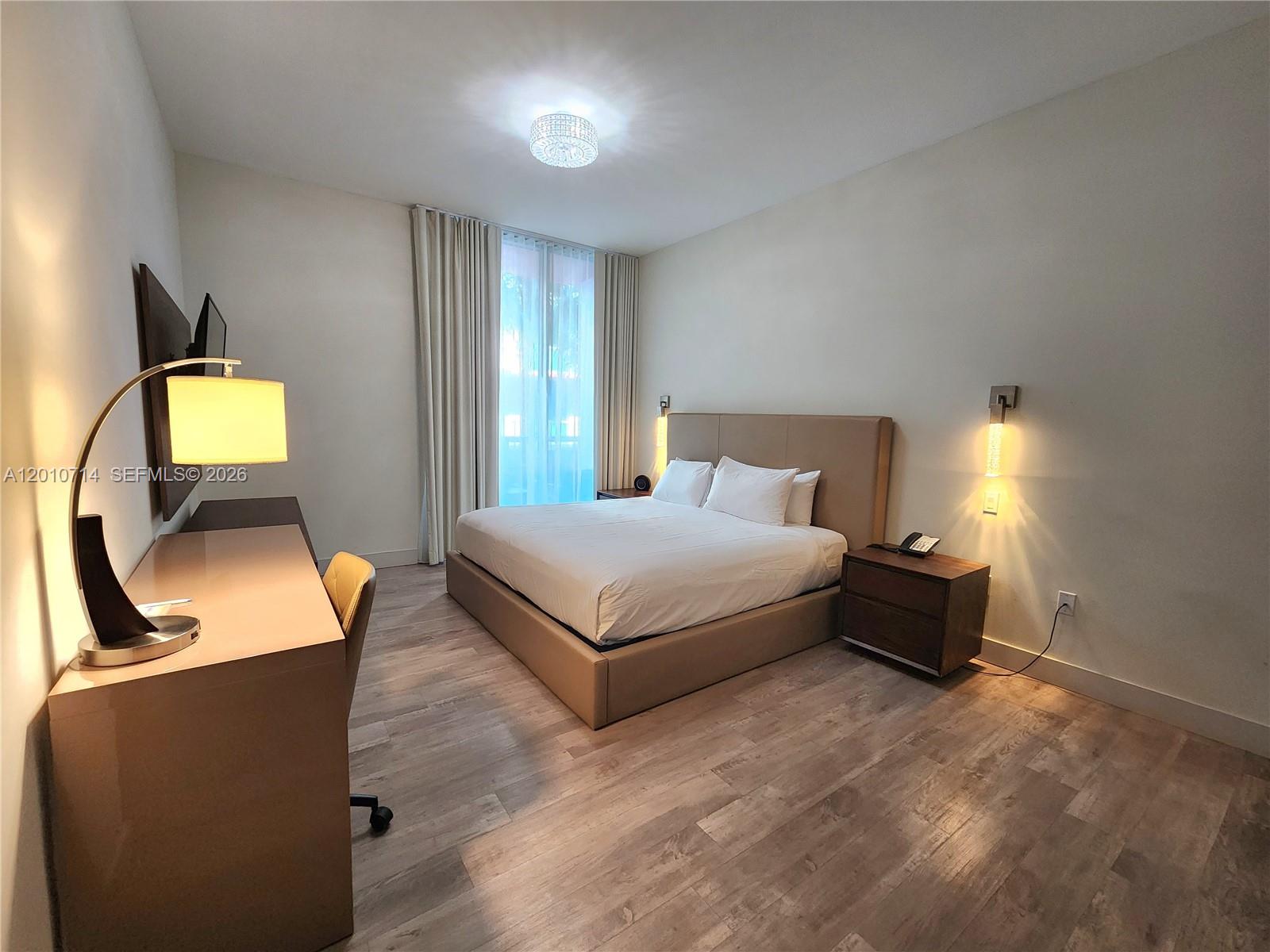 A modern bedroom features a king bed, a desk, and wood-look flooring — 777 N Ocean Dr # S207, Hollywood FL 33019, HOLLYWOOD, FL