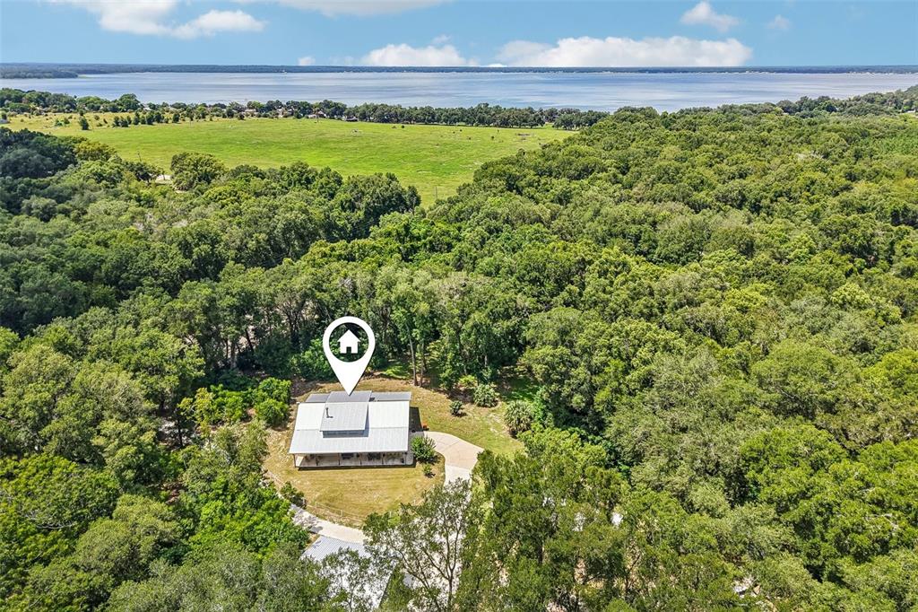 An aerial view shows a house with a metal roof surrounded by dense forest — 16161 SE 137TH COURT, WEIRSDALE, FL