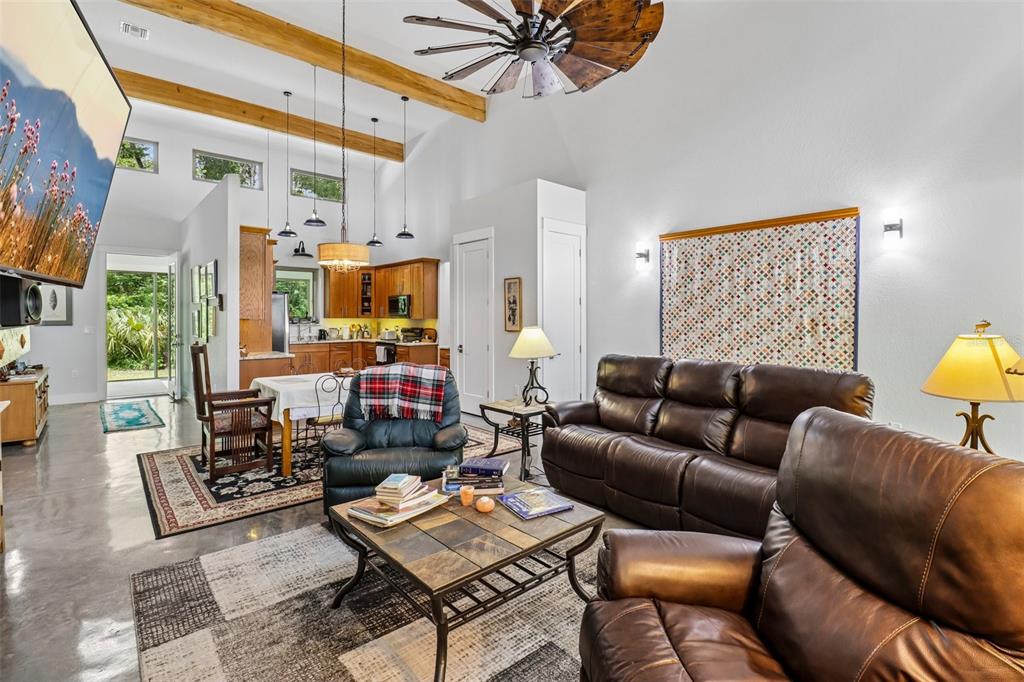 A living room with a stone fireplace, vaulted ceiling, and an open kitchen in back — 16161 SE 137TH COURT, WEIRSDALE, FL