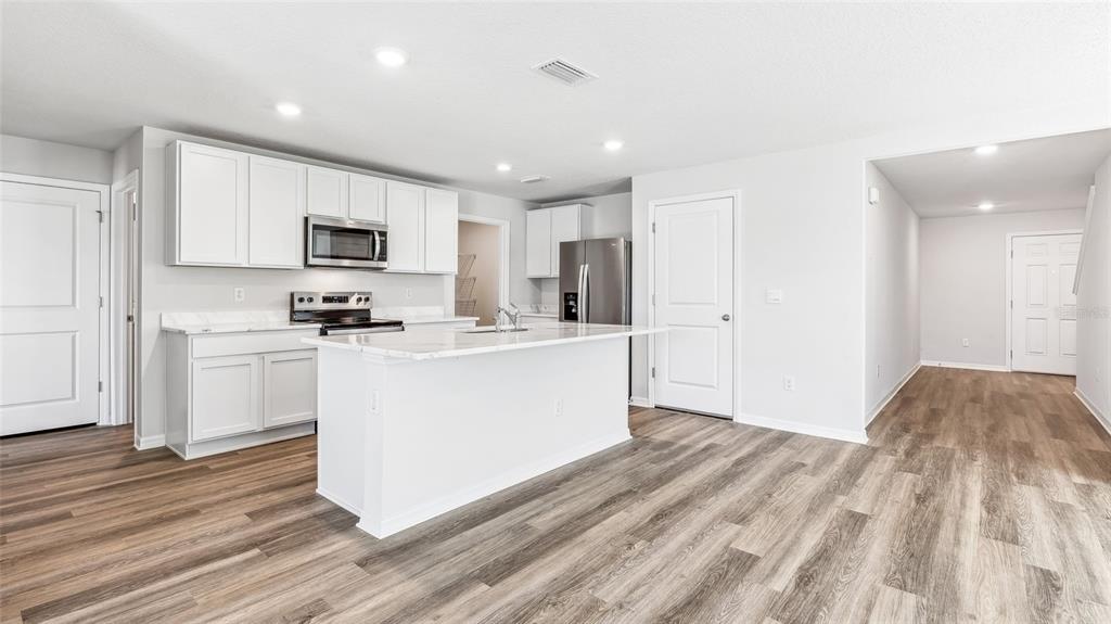 A modern kitchen features white cabinets, stainless steel appliances, a marble-topped island, and wood-look flooring — 8837 CLEAR VIEW STREET, PARRISH, FL