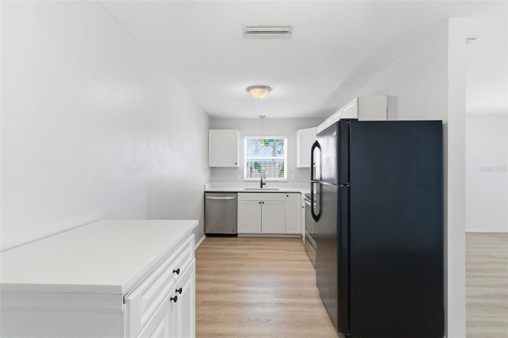 A kitchen features white cabinets, stainless steel appliances, a black refrigerator, and light wood flooring — 2227-2229 MONTCLAIR DRIVE UNIT 1&2, SARASOTA, FL