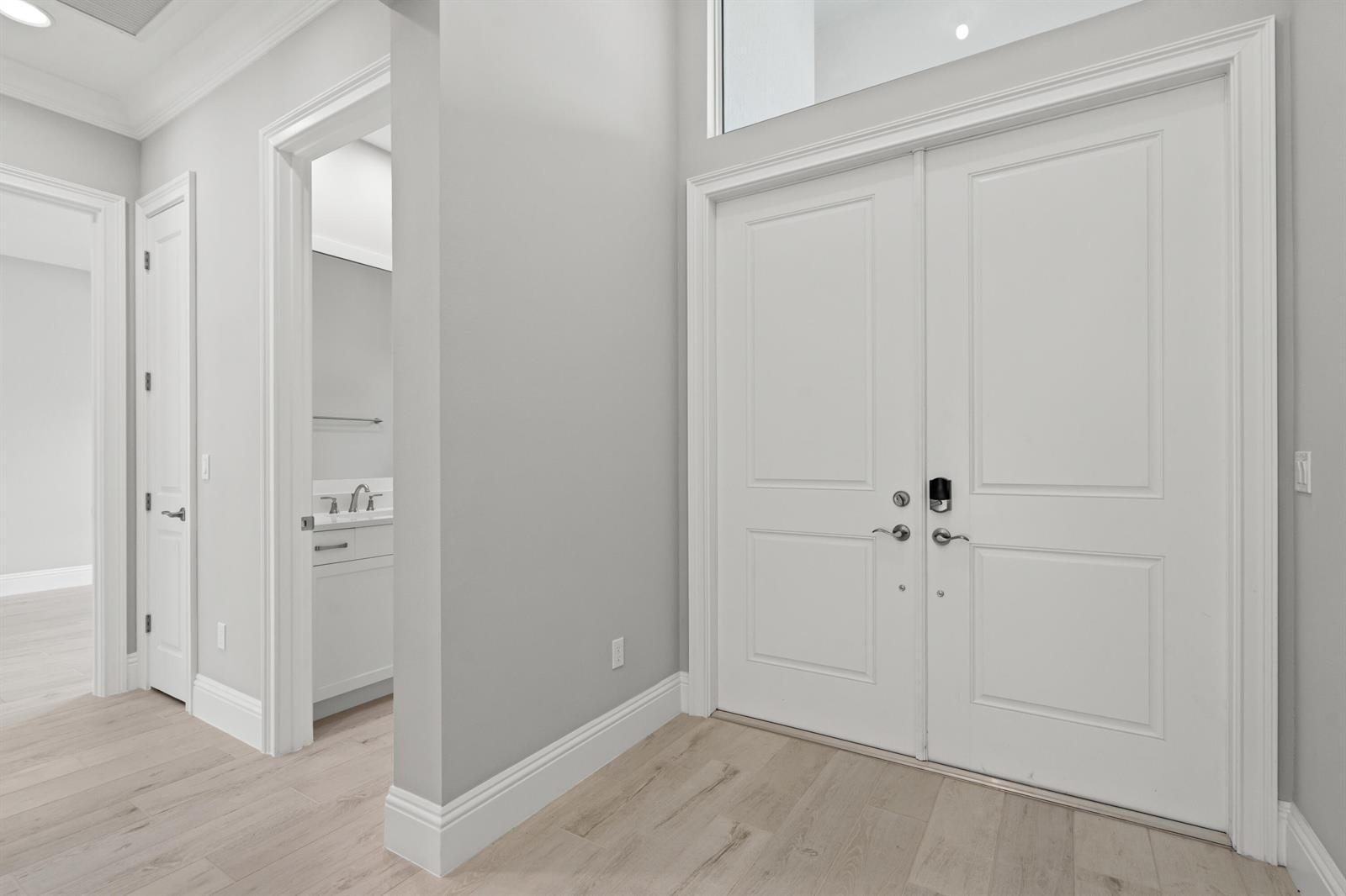 A bright entryway features light wood floors, white double doors, and an adjacent bathroom doorway — 4133 Lucaya Pointe Way, Vero Beach FL 32967, VERO BEACH, FL