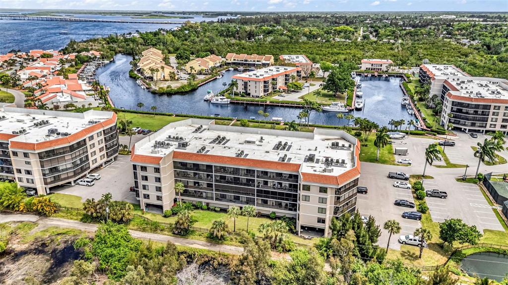 An aerial view shows several multi-story apartment buildings with red tile roofs near a canal — 25188 MARION AVENUE UNIT E212, PUNTA GORDA, FL