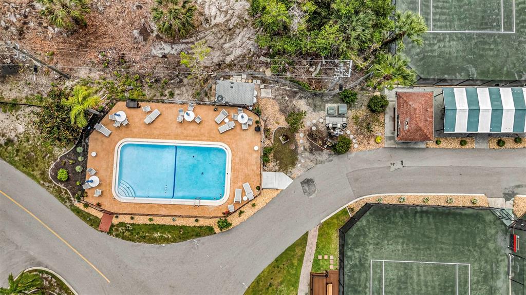 An aerial view shows a swimming pool, lounge chairs, and two tennis courts — 25188 MARION AVENUE UNIT E212, PUNTA GORDA, FL