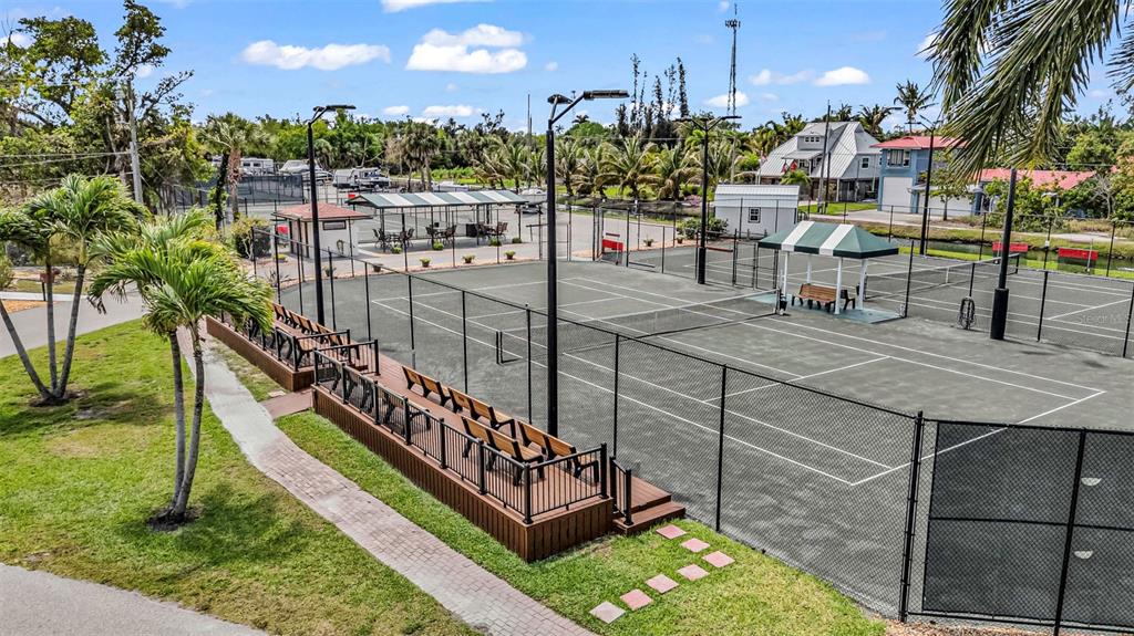 An elevated view of a fenced tennis court with spectator seating and a shaded bench — 25188 MARION AVENUE UNIT E212, PUNTA GORDA, FL