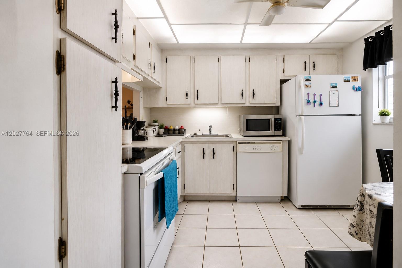 A kitchen features white cabinets, white appliances, tiled flooring, and a drop ceiling with lighting — 3050 Holiday Springs Blvd # 305, Margate FL 33063, MARGATE, FL
