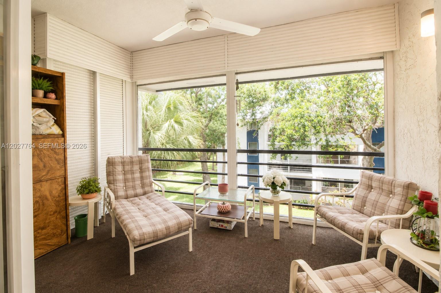 A sunroom with plaid chairs, a wooden shelving unit, and large windows overlooking trees — 3050 Holiday Springs Blvd # 305, Margate FL 33063, MARGATE, FL
