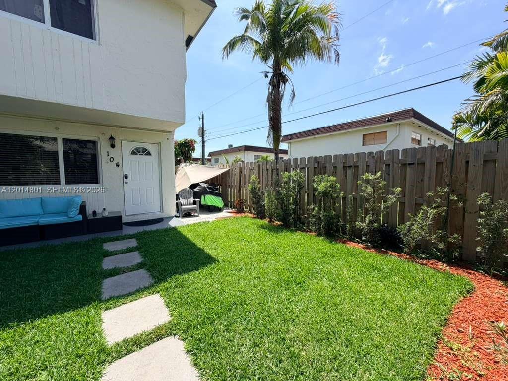 A white two-story building features a small fenced backyard with a lawn and patio — 1500 NE 151st St # 104, Miami FL 33162, MIAMI, FL
