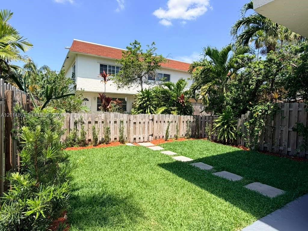 A backyard with a green lawn, stone path, and wooden fence facing a two-story building — 1500 NE 151st St # 104, Miami FL 33162, MIAMI, FL