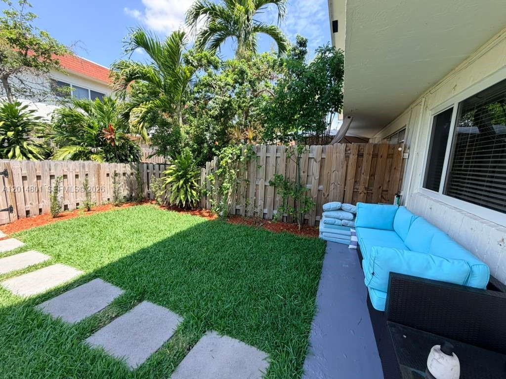 A small backyard features a green lawn, stone pavers, a wooden fence, and a blue sofa — 1500 NE 151st St # 104, Miami FL 33162, MIAMI, FL
