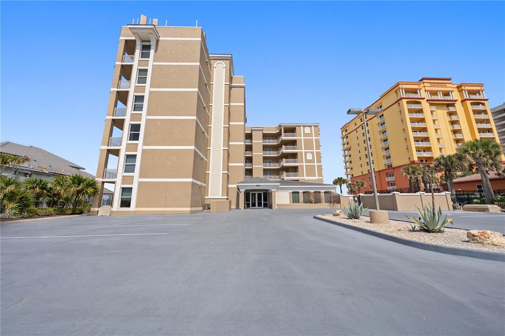 A multi-story tan building with a parking lot and a yellow building in the background — 2855 S ATLANTIC AVENUE UNIT 201, DAYTONA BEACH, FL