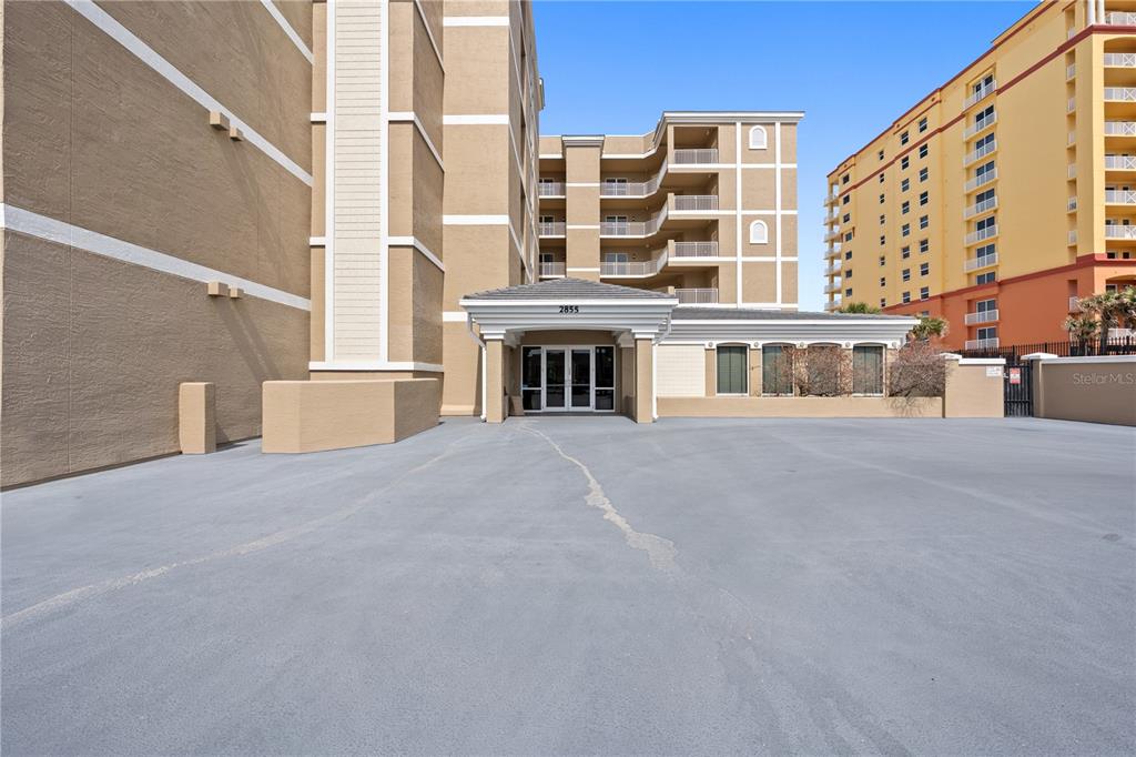 The exterior of a tan multi-story building features a covered entrance and a paved lot — 2855 S ATLANTIC AVENUE UNIT 201, DAYTONA BEACH, FL