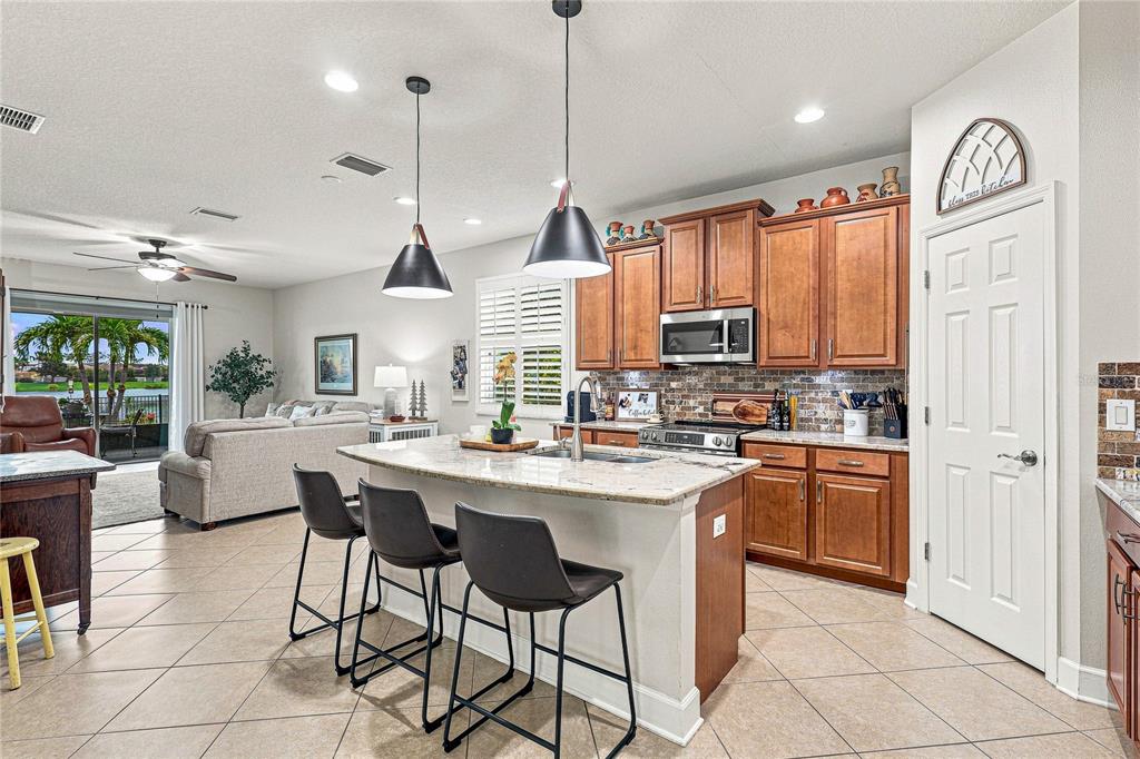 A kitchen with wood cabinets, granite countertops, and a center island with three bar stools — 8478 NANDINA DRIVE, SARASOTA, FL