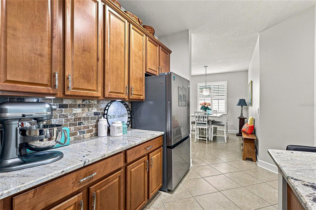 A kitchen with wood cabinets, granite countertops, and a stainless steel refrigerator leads to a dining area — 8478 NANDINA DRIVE, SARASOTA, FL