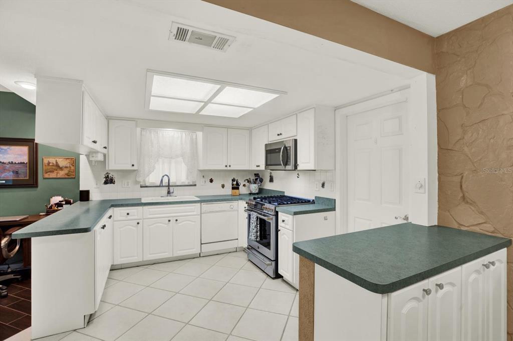 A kitchen features white cabinets, green countertops, a gas range, and a tile floor — 5790 150TH AVENUE N, CLEARWATER, FL