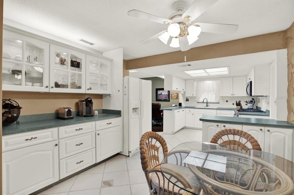 A kitchen features white cabinetry, green countertops, a glass dining table, and a ceiling fan — 5790 150TH AVENUE N, CLEARWATER, FL