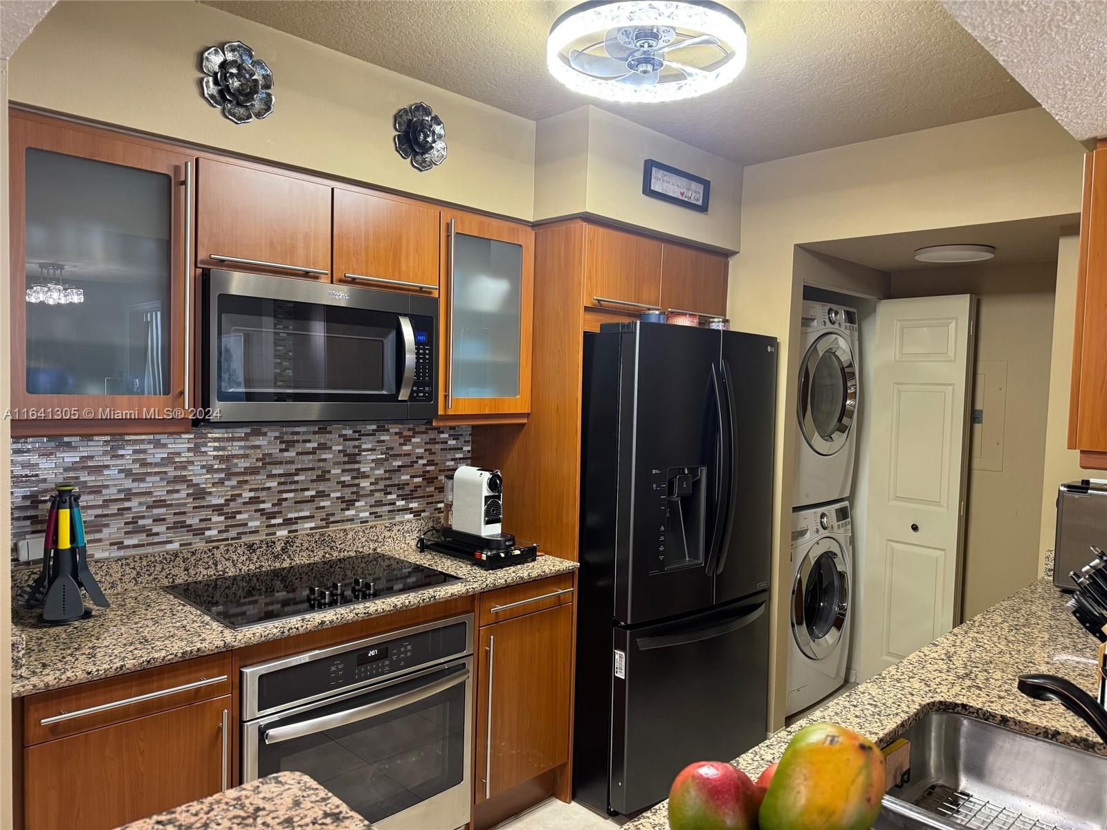 A kitchen features wood cabinets, granite countertops, stainless steel appliances, and a stacked laundry unit — 2080 S Ocean Dr # 1607, Hallandale Beach FL 33009, HALLANDALE BEACH, FL