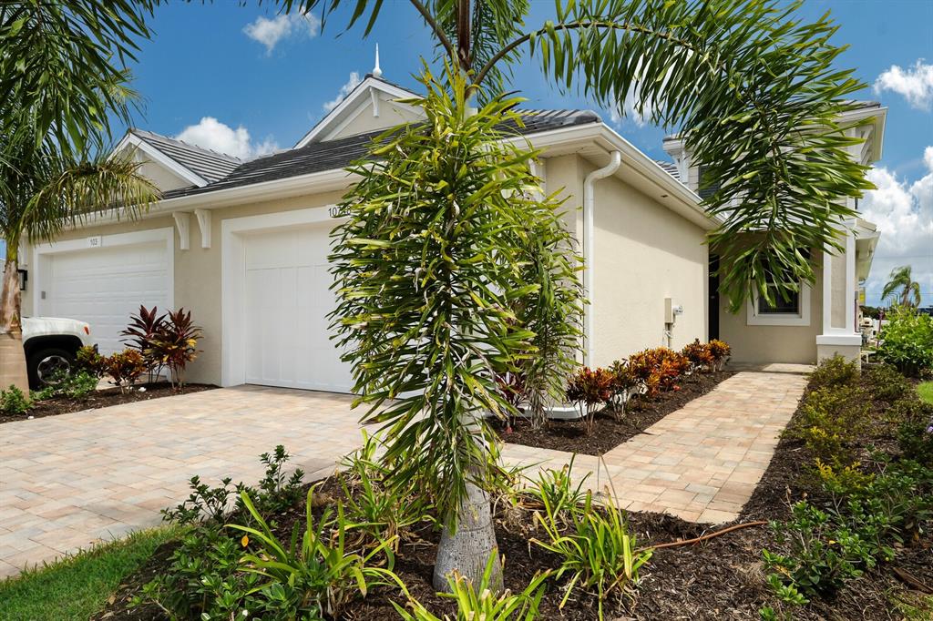 A beige house exterior features a paved driveway, a two-car garage, and tropical landscaping — 10748 KLEE AVENUE, BRADENTON, FL