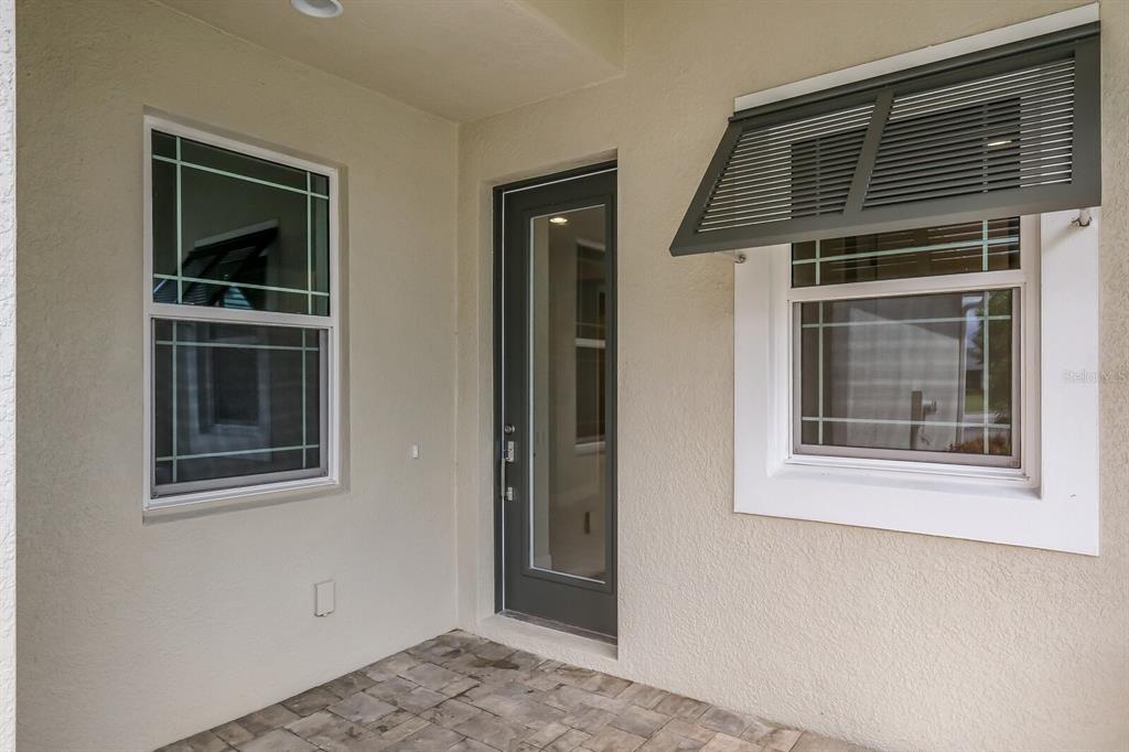 A covered patio features a glass door, two windows with grilles, and stone paver flooring — 10748 KLEE AVENUE, BRADENTON, FL