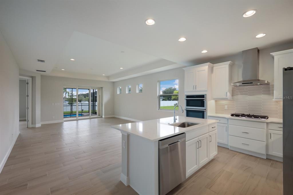 A modern kitchen with white cabinets and an island overlooks an open living area — 10748 KLEE AVENUE, BRADENTON, FL