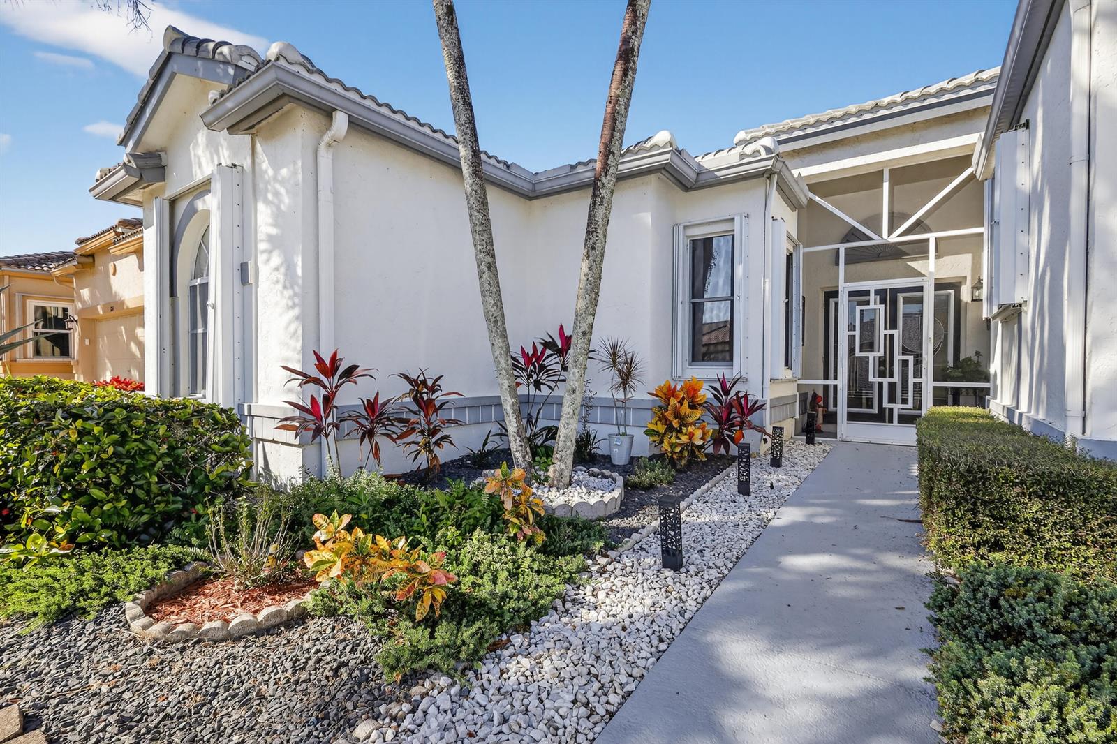 The exterior of a stucco home features a white screened entryway and landscaped front yard — 3747 Spring Crest Court, Lake Worth FL 33467, LAKE WORTH, FL
