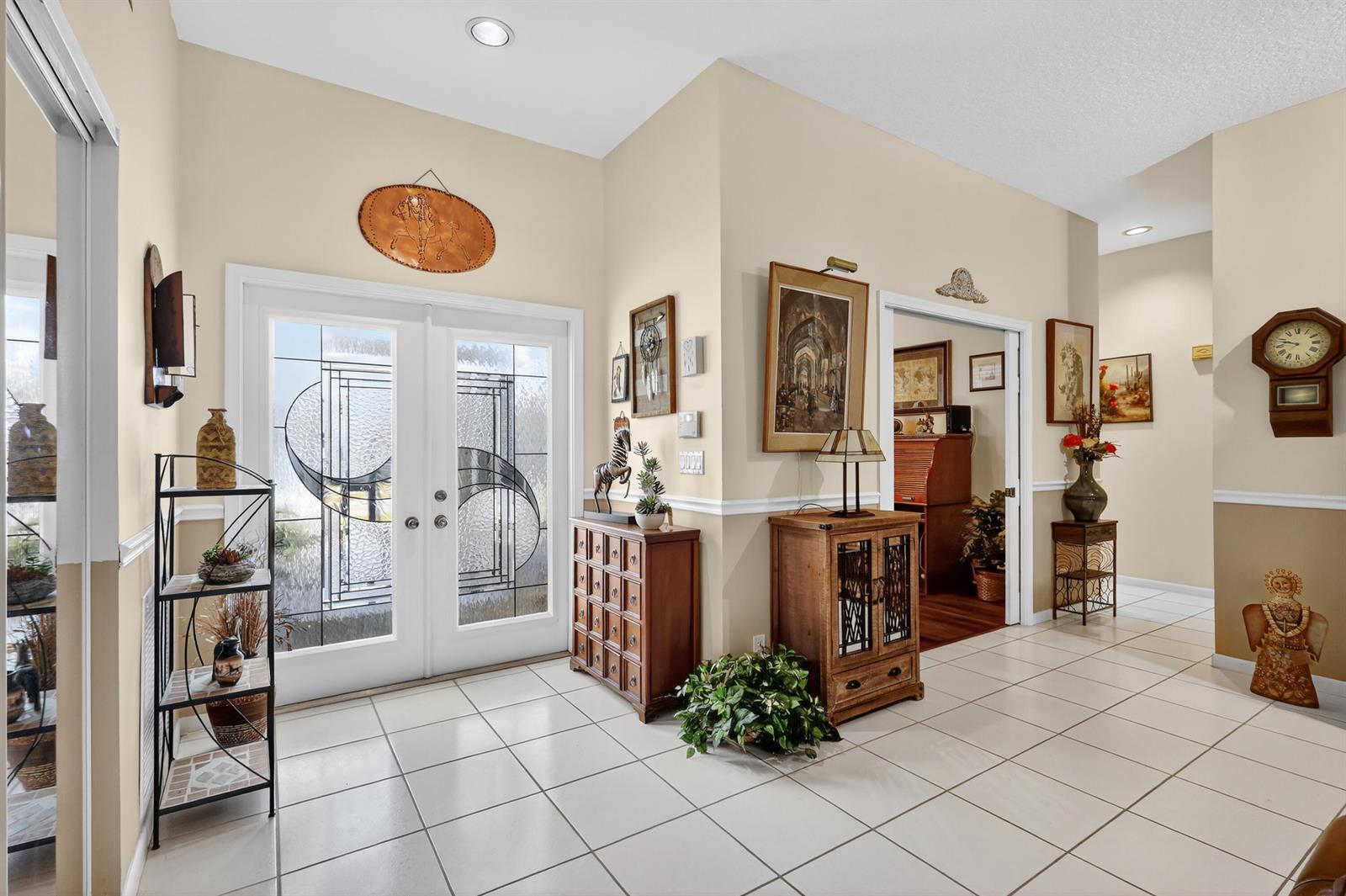 A tiled entryway features double glass-paneled doors, wooden furniture, wall art, and a wall clock — 3747 Spring Crest Court, Lake Worth FL 33467, LAKE WORTH, FL