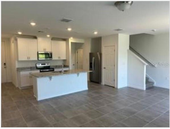 A kitchen with white cabinets, a central island, and stainless steel appliances on tiled floors — 4325 EAGLE TRAIL BEND, ST CLOUD, FL