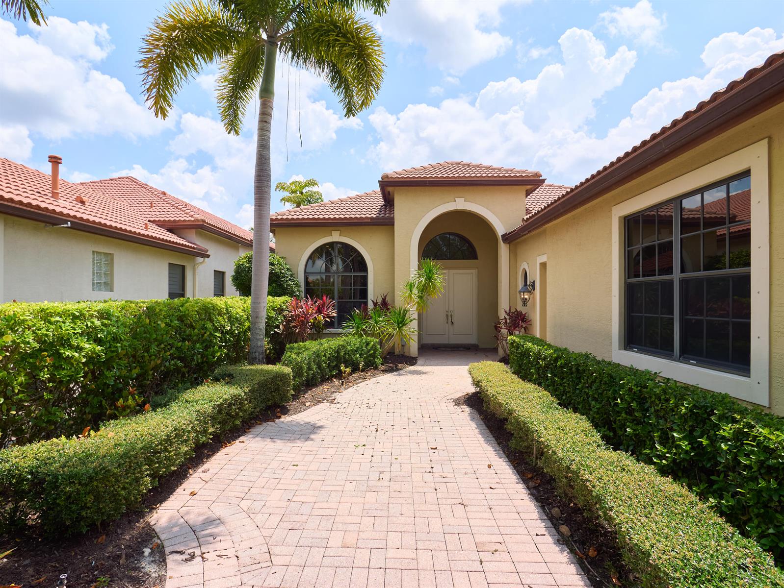 A paved walkway leads to the arched entryway of a tan stucco house with palm trees — 6490 Sparrow Hawk Drive, West Palm Beach FL 33412, WEST PALM BEACH, FL