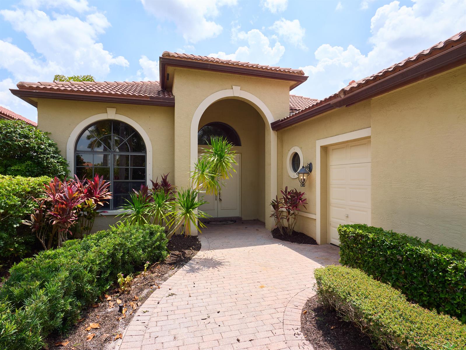 The exterior of a tan stucco house features a tiled roof, arched entryway, and landscaping — 6490 Sparrow Hawk Drive, West Palm Beach FL 33412, WEST PALM BEACH, FL