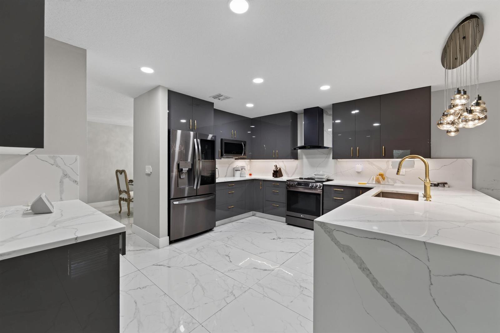 A modern kitchen features dark glossy cabinets, white marble-patterned countertops, and a matching tiled floor — 6544 Adriatic Way, FL 33413, FL