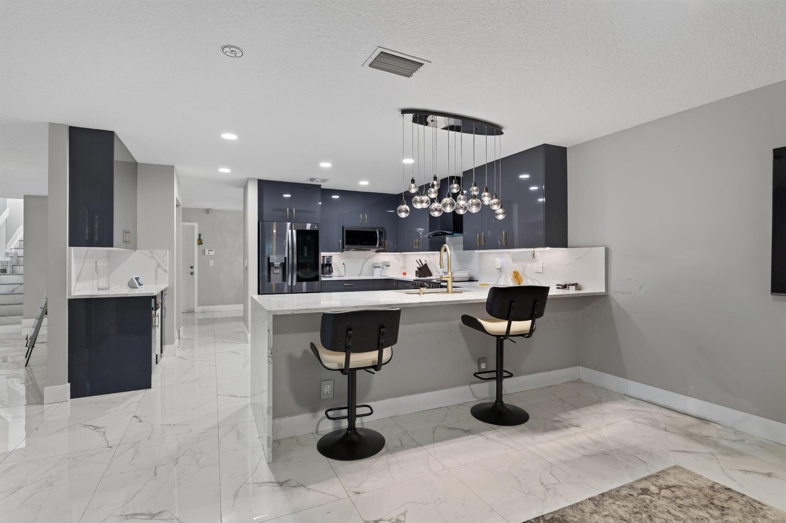 A modern kitchen features dark glossy cabinets, white marble countertops, and a matching breakfast bar — 6544 Adriatic Way, FL 33413, FL
