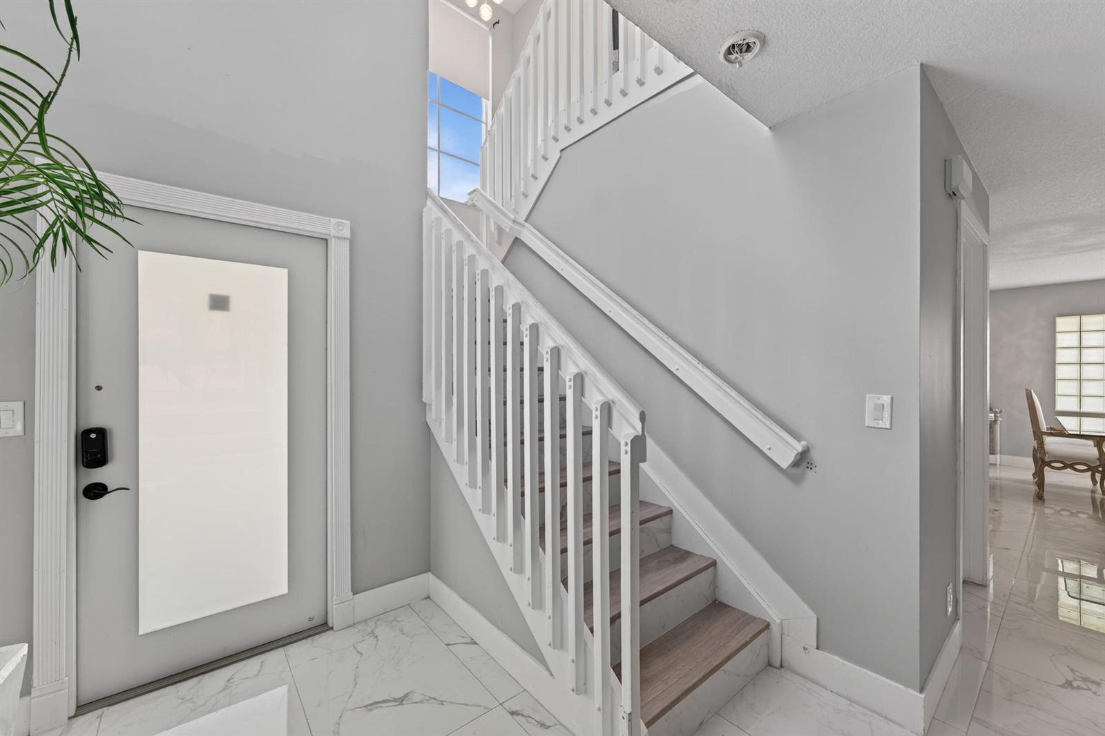 A bright entryway features a white staircase, marble-look tile flooring, and a modern front door — 6544 Adriatic Way, FL 33413, FL