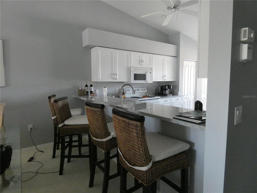 A kitchen with white cabinets, a breakfast bar, and three wicker bar stools — 4639 CHAPEL HILL DRIVE UNIT 2923, SARASOTA, FL