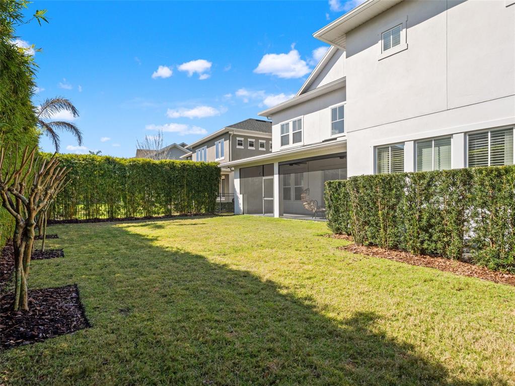 A backyard features a grassy lawn, a screened-in patio, and tall privacy hedges — 12515 BOVET AVENUE, ORLANDO, FL
