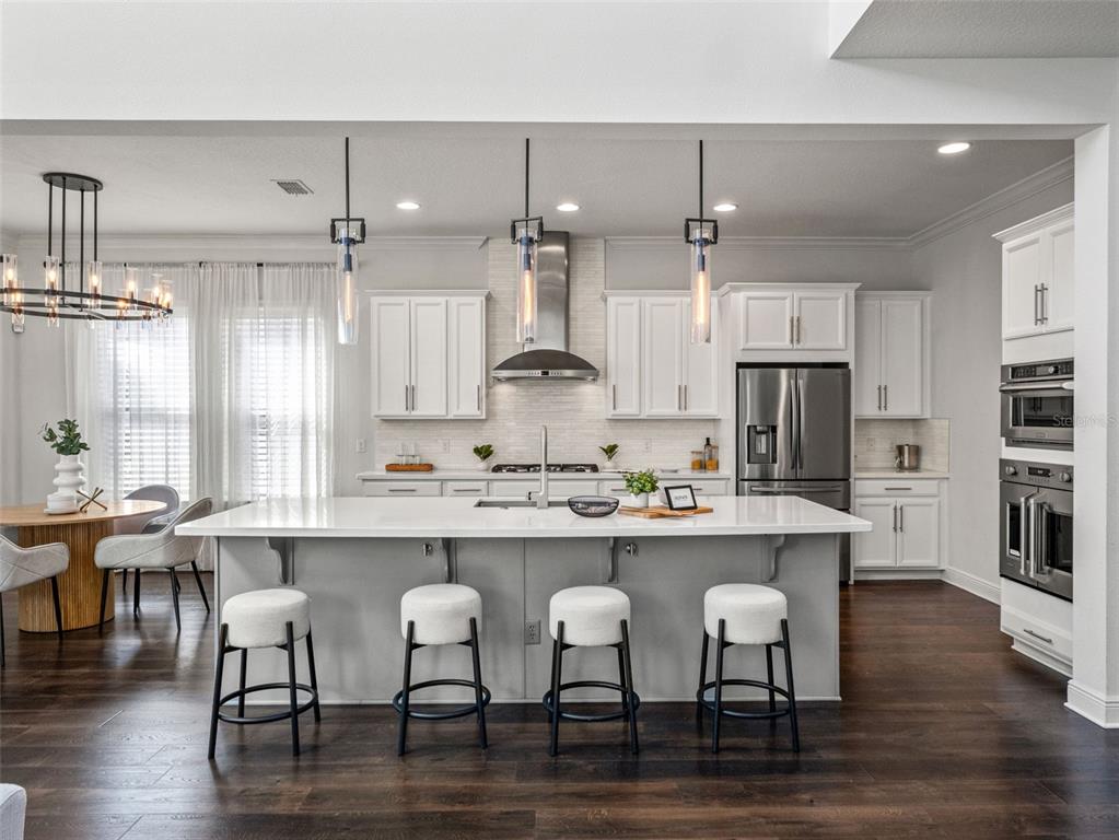 A modern kitchen features white cabinetry, a large central island with seating, and dark flooring — 12515 BOVET AVENUE, ORLANDO, FL