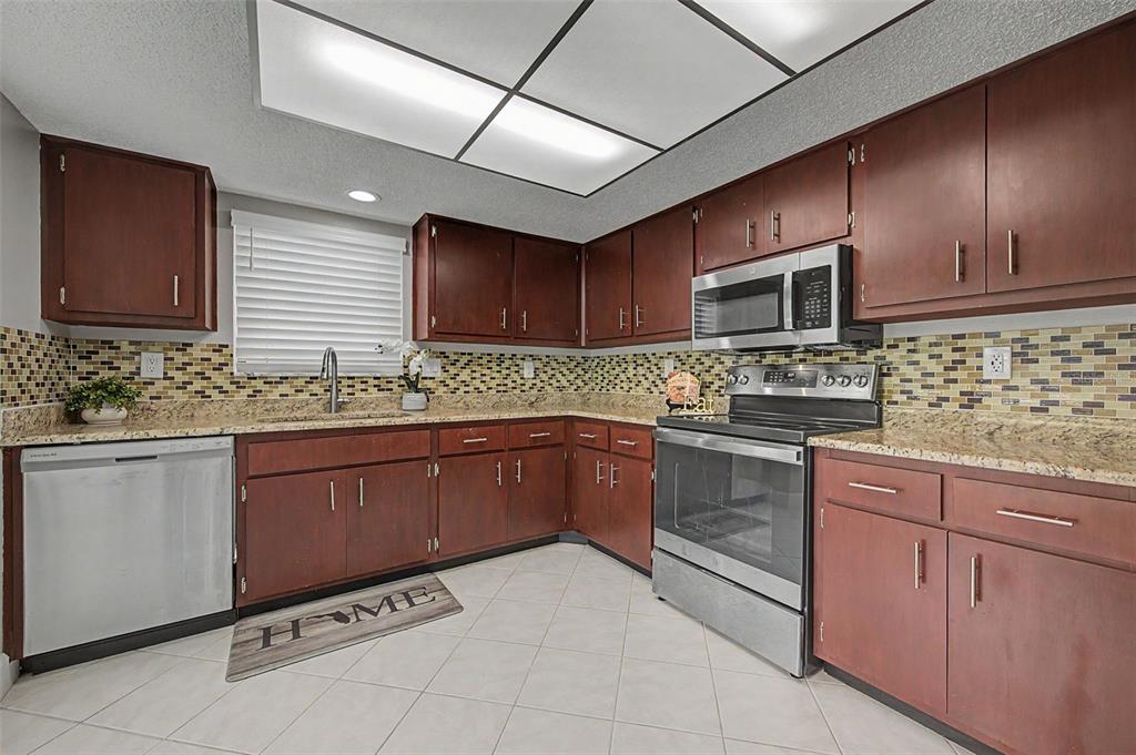 A kitchen features dark wood cabinets, stainless steel appliances, granite countertops, and a tiled backsplash — 7800 FAIRLAWN DRIVE, HUDSON, FL