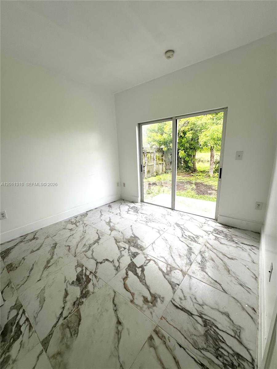 An empty room features white marble-patterned tile flooring and a sliding glass door — 2514 NE 41st Ave, Homestead FL 33033, HOMESTEAD, FL