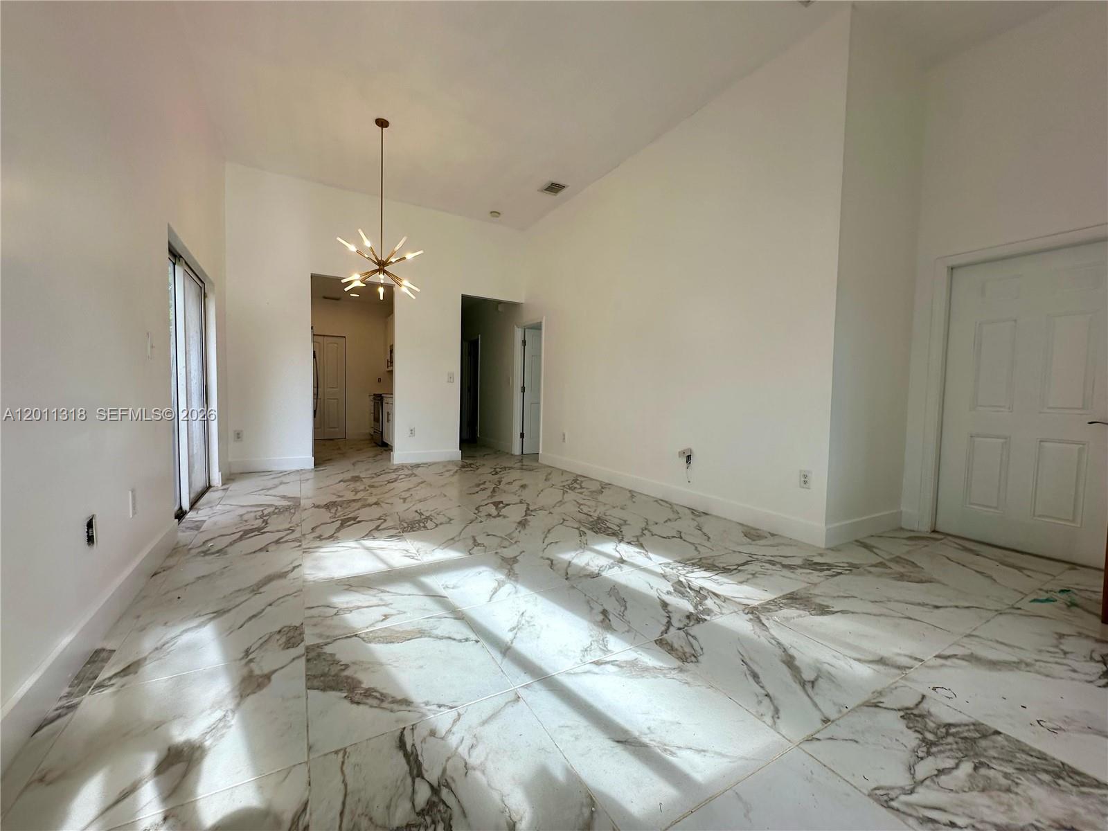 A bright room features white marble-look tile flooring, a modern chandelier, and high ceilings — 2514 NE 41st Ave, Homestead FL 33033, HOMESTEAD, FL