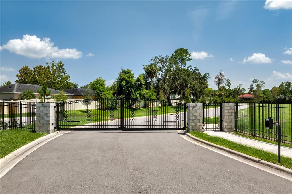 A paved road leads to a closed black metal gate flanked by stone pillars — 950 FRIENDS COURT, SANFORD, FL