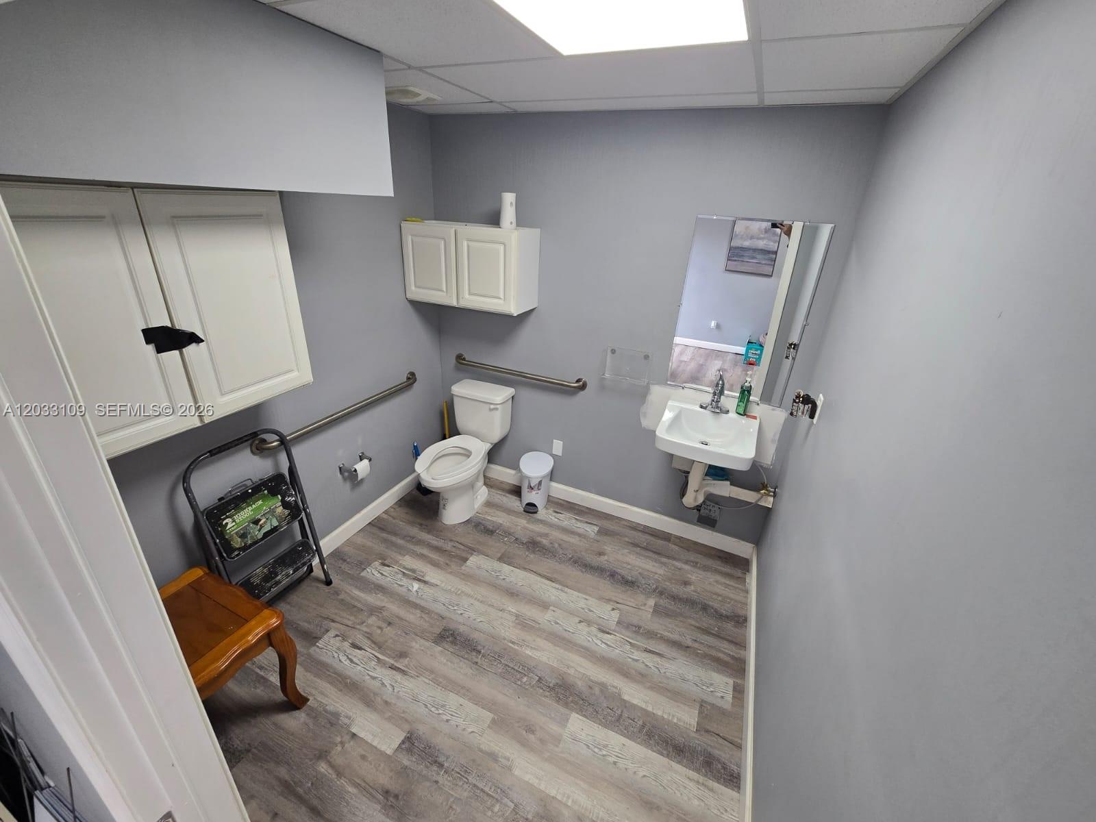A gray-walled accessible restroom features a toilet, wall-mounted sink, and wood-look vinyl flooring — 535 N State Road 7, Margate FL 33063, MARGATE, FL
