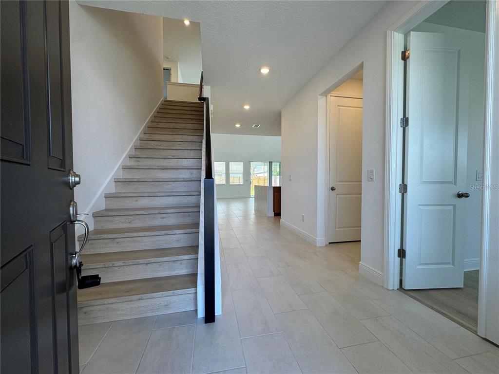 An entryway features a staircase with wood-look treads, light tile flooring, and white walls — 19141 PLANETREE STREET, ORLANDO, FL