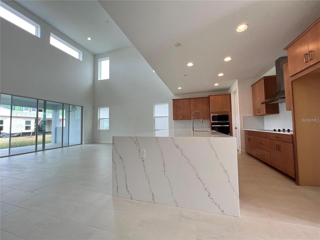A modern kitchen features a large quartz waterfall island, wood cabinetry, and high ceilings — 19141 PLANETREE STREET, ORLANDO, FL