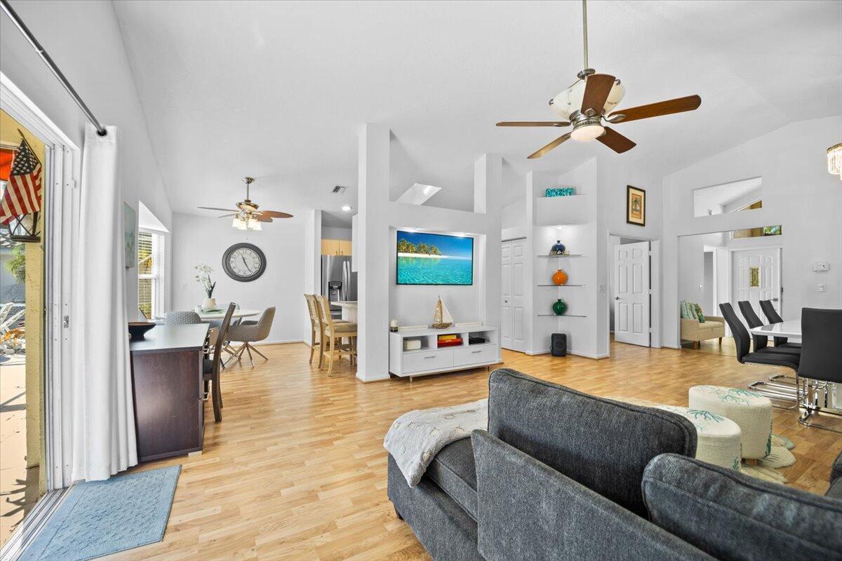 An open-concept living and dining area features light wood flooring, a ceiling fan, and television — 7534 Ironbridge Circle, Delray Beach FL 33446, DELRAY BEACH, FL